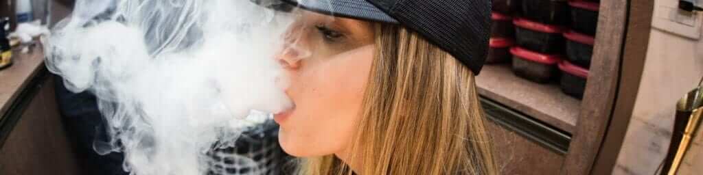 girl in hat blowing vape smoke